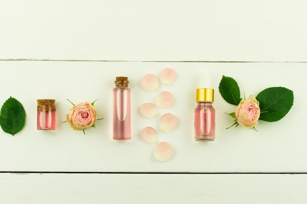 Top view of the white wooden background with cosmetic bottles with rose oil and rose water for facial care. flat lay.