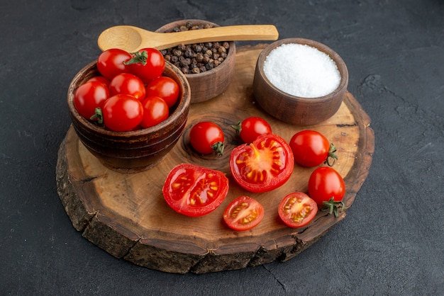 Top view of whole cut fresh tomatoes and spices on wooden board on black surface