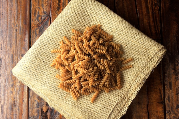 Top view of the whole mass of Fusilli, on fabric, rustic towel with wooden spoon, on a wooden background. copy space