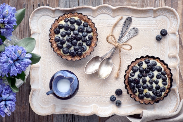 Top view on wholegrain blueberry tarts with vanilla cream on a ceramic tray