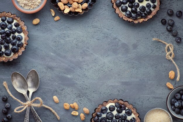 Photo top view on wholegrain blueberry tarts with vanilla cream on dark background