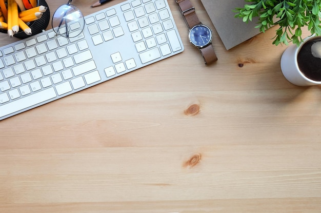 Вид сверху на беспроводную клавиатуру, чашку кофе, очки, ноутбук и комнатное растение на деревянном столе