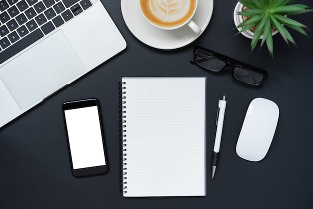 Top view with laptop, mobile phone, coffee cup, pencil, pencil and glasses placed on black