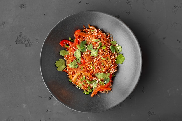 Top view of wok noodles with vegetables and meat in bowl on gray background