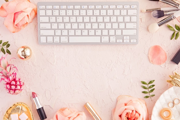 Top view of woman beauty blogger working desk with computer keyboard and laptop, decorative cosmetic, flowers and palm leaves