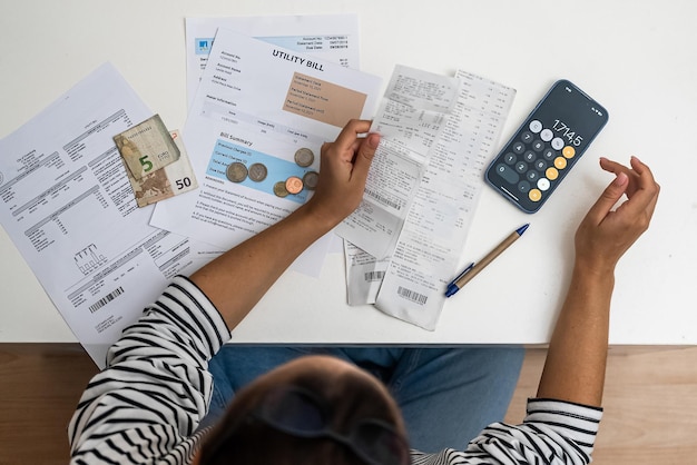 Top view woman counts utility and bank bills sitting on floor smartphone calculator and documents