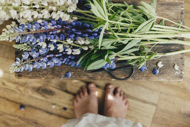 Top view of woman feet and beautiful lupine flowers in rustic room arranging home decor