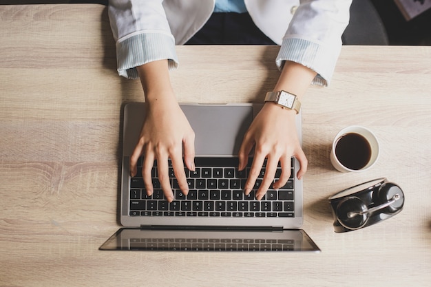 Top view of woman hand typing on laptop keyboard on a wooden office desk