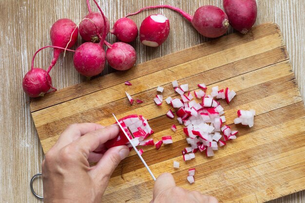 Top view of woman hands cutting unpeeled radish on the wooden background