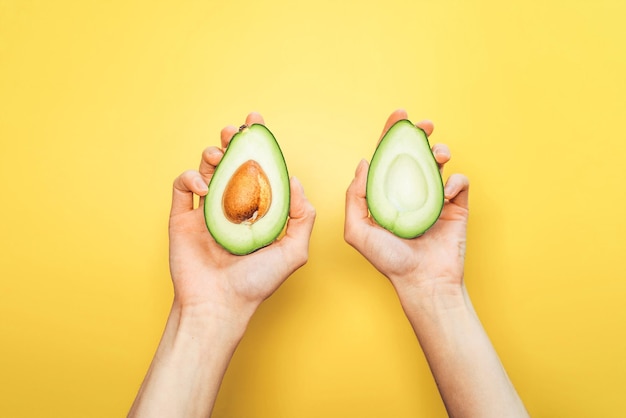 Photo top view of woman hands holding avocado on yellow background