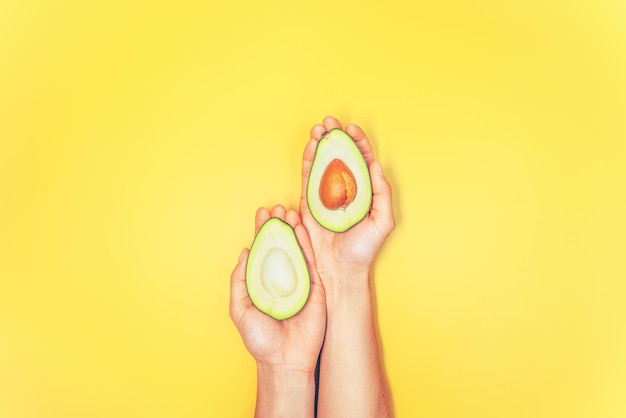 Top view of woman hands holding avocado on yellow background