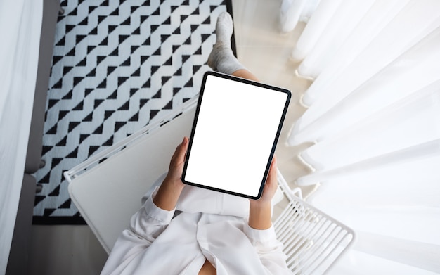 Top view  of a woman holding black tablet pc with blank white desktop screen while sitting in bedroom with feeling relaxed in the morning