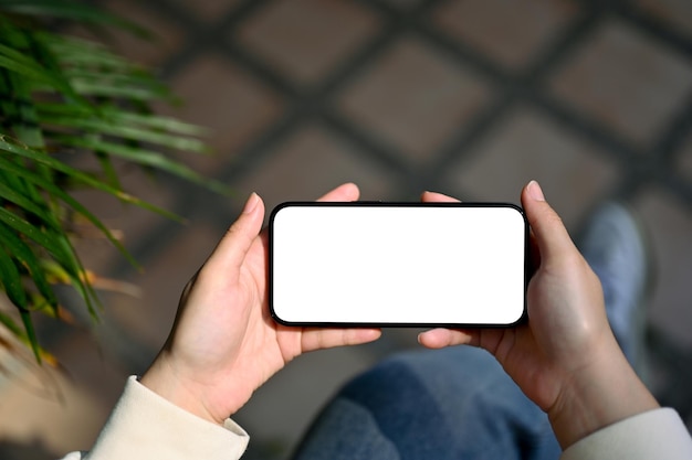 Top view of a woman holding a smartphone white screen mockup in a horizontal position