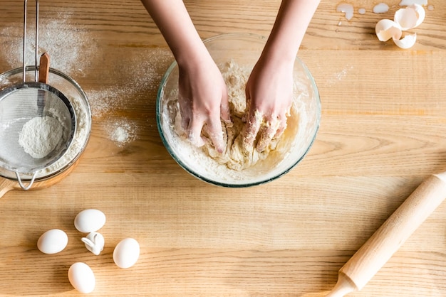 Top view of woman kneading dough near flour in bowl eggs and figurine with easter bunny