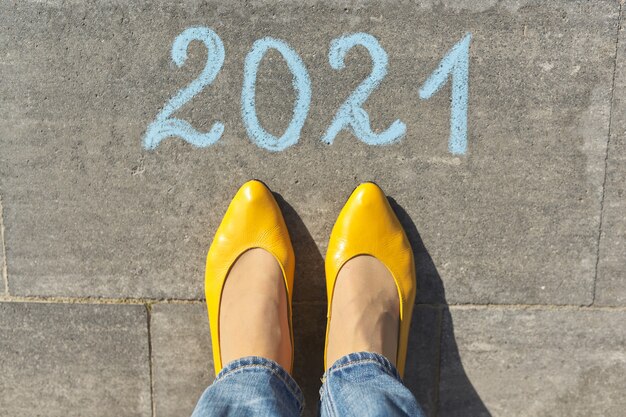 top view on woman legs and 2021 text written in chalk on gray sidewalk