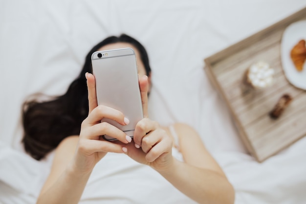 Vista dall'alto della donna sdraiata a letto con lo smartphone