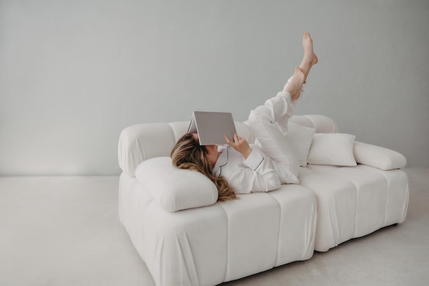 Вид сверху на женщину, лежащую на диване с книгой
