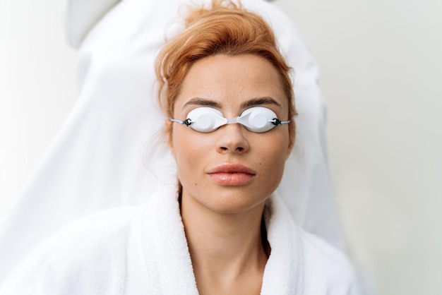 Top view of the woman patient wearing protective googles laying at the couch after hair removal procedure at the clinic