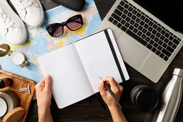 Photo top view woman planning a trip with a map and laptop, writing in a notebook