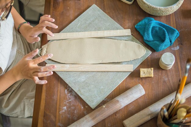 Top view woman potter working on potters wheel making ceramic
pot from clay in pottery workshop focus hand young woman attaching
clay product part to future ceramic product pottery workshop