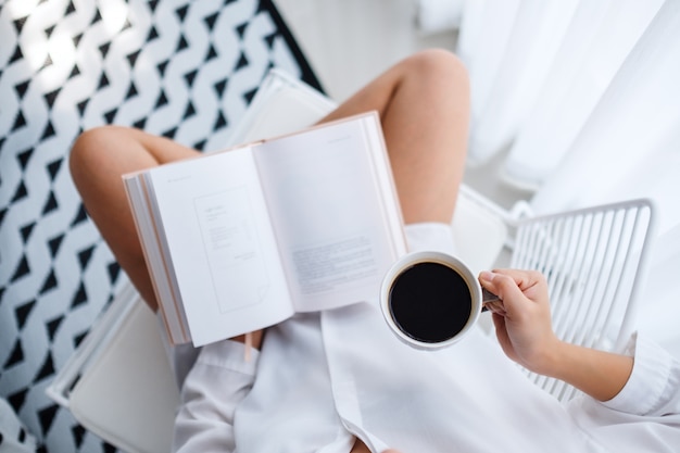 Top view  of a woman reading book and drinking hot coffee in bedroom at home in the morning