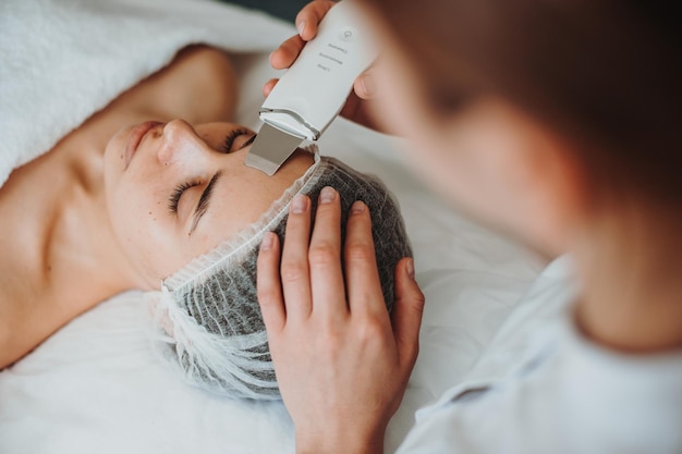 Top view of a woman receiving ultrasound cavitation facial peeling in spa salon happy face cosmetolo