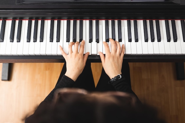 Top view of woman\'s hands playing piano by reading sheet\
music.