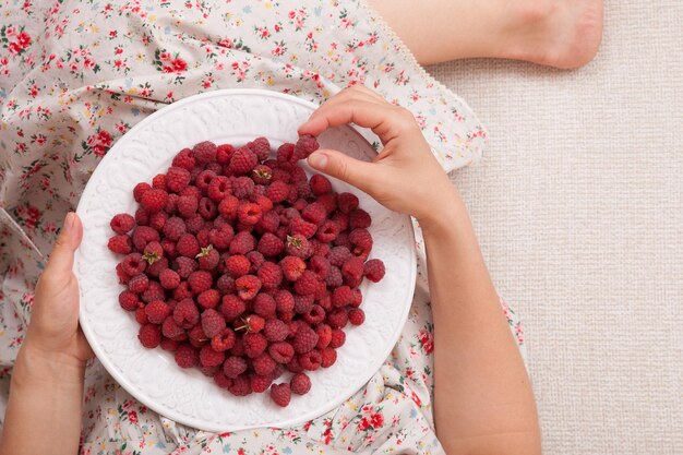 Top view on woman sitting cozy on the couch and enjoying delicious summer organic raspberries