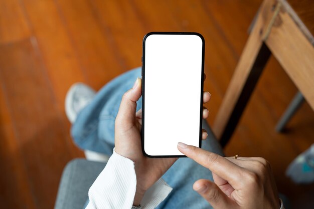 Top view of a woman using her smartphone while sitting indoors A whitescreen smartphone mockup