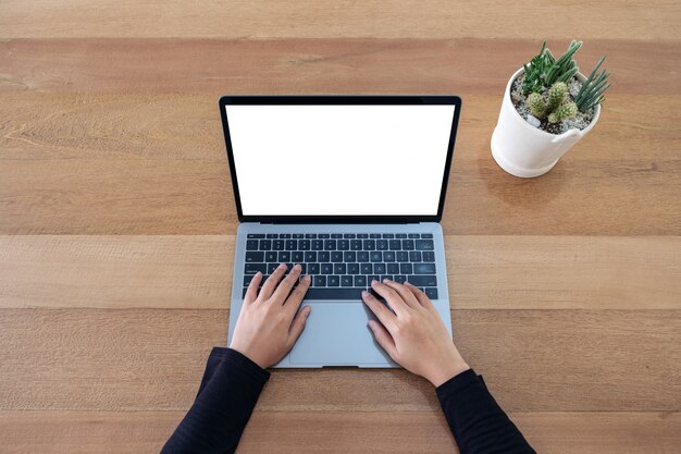 Foto vista dall'alto di una donna che utilizza e digita sul computer portatile con schermo bianco vuoto e vaso di cactus sul fondo della tavola in legno