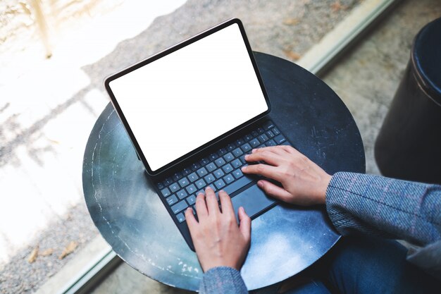 Top view  of a woman using and typing on tablet keyboard with blank white desktop screen as a computer pc on the table