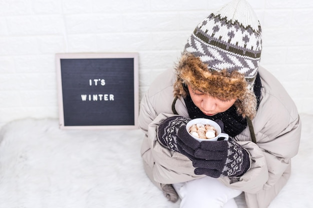 Top view of woman wearing puffer jacket and knitted beanie hat enjoying hot drink at winter time