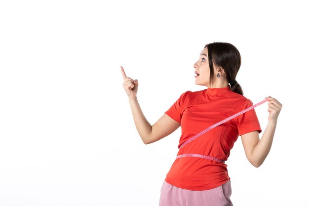 Top view of a wondering young lady gathering her hair dressed in redorange blouse and holding metre measuring her waist pointing up on white background