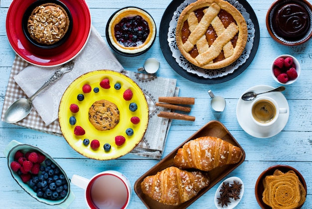 Foto vista dall'alto di un tavolo di legno pieno di torte, frutta, caffè, biscotti, spezie e altro ancora