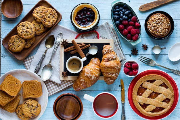 Top view of a wood table full of cakes, fruits, coffee, biscuits, spices and more