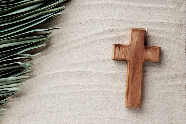 Photo top view wooden cross and leaf on sand