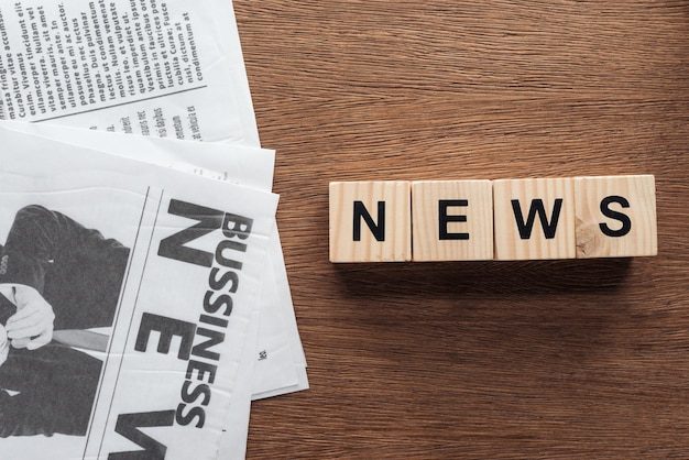 Top view of wooden cubes with word news and business newspapers on wooden tabletop