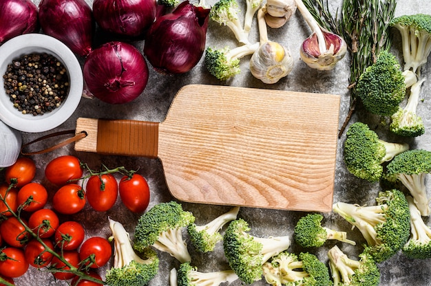 Top view of Wooden cutting Board  among uncooked vegetables. Concept of home vegetarian cuisine