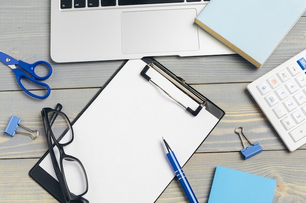 Top view of wooden desktop with glasses and stationery items close up. Mock up