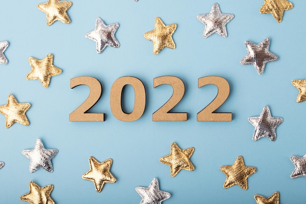 파란색 배경에 있는 나무 숫자 2022의 상위 뷰Festive 개념 주위의 황금색 및 은색 별