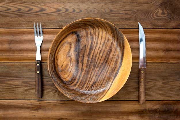 Top view of wooden roud plate with fork and knife, on wooden table. Copy space, menu, recipe or dieting concept.