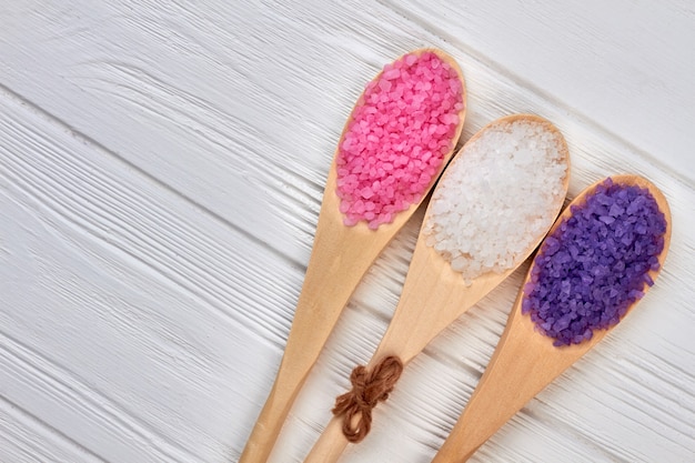 Top view wooden spoons with colored salt on white desk.