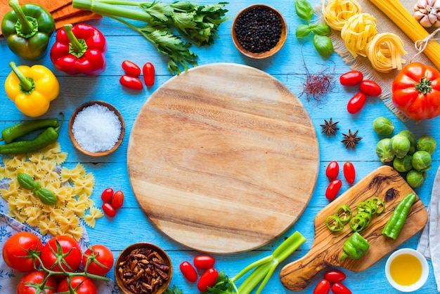 Top view of a wooden table full of italian pasta ingradients like peppers, tomatoes, olive oil, basi