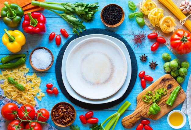 Top view of a wooden table full of italian pasta ingradients like peppers, tomatoes, olive oil, basi