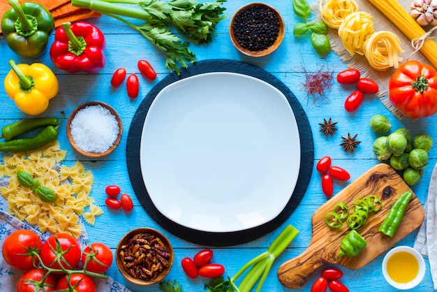 Top view of a wooden table full of italian pasta ingradients like peppers, tomatoes, olive oil, basi