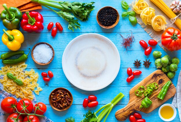 Top view of a wooden table full of italian pasta ingradients like peppers, tomatoes, olive oil, basi