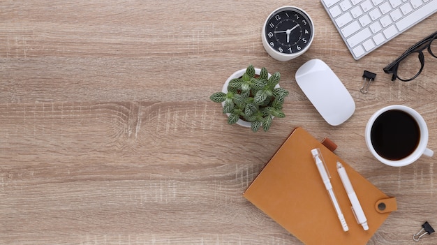 Top view wooden workspace office desk with computer and office supplies. Flat lay work table with blank notebook, keyboard, pen , smartphone and coffee cup. Copy space for your advertising content.