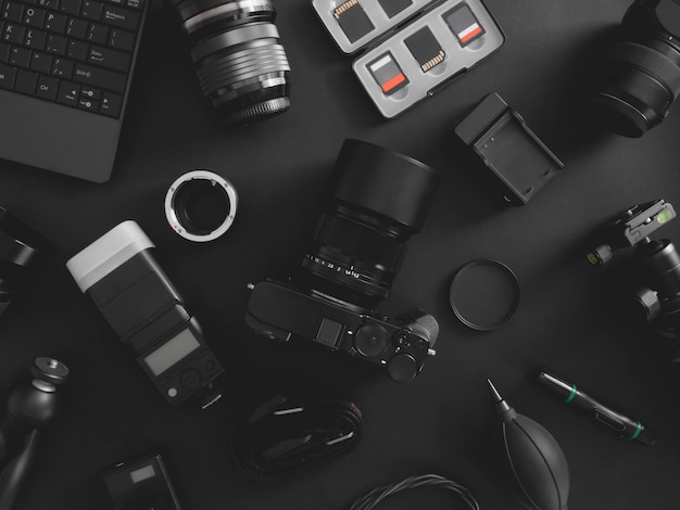 Vista dall'alto del fotografo dello spazio di lavoro con fotocamera digitale, flash, kit di pulizia, memory card, treppiede e accessorio per fotocamera su sfondo nero da tavolo