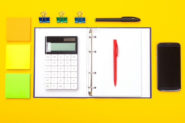 Top view of working space table with mobile phone, notebook and pen isolated  yellow  