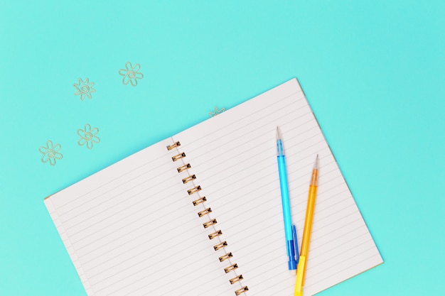 Top view of working table with open copybook on spring, yellow colored pencil,  golden metal clips for paper and documents. Flat lay with stationery for school, education.